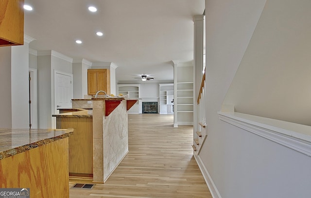 kitchen with crown molding, ceiling fan, light stone counters, and light hardwood / wood-style flooring