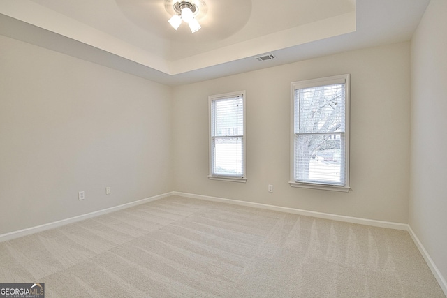 unfurnished room with a raised ceiling, light carpet, and ceiling fan