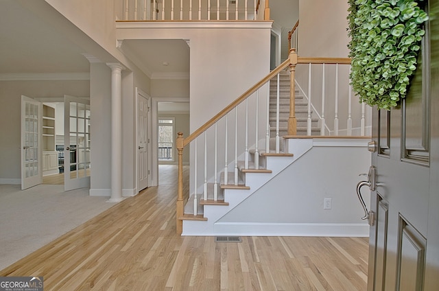 entryway featuring decorative columns, ornamental molding, a towering ceiling, and light hardwood / wood-style floors