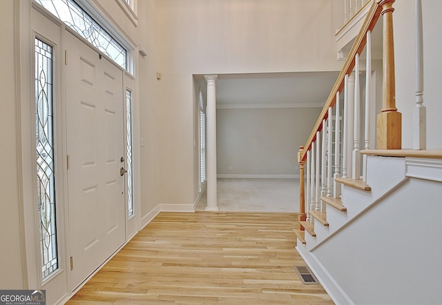 foyer with a towering ceiling, ornamental molding, light hardwood / wood-style floors, and decorative columns