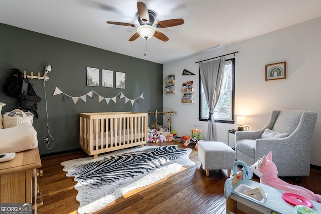 bedroom with dark hardwood / wood-style flooring, a nursery area, and ceiling fan