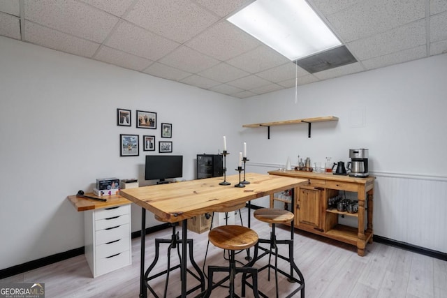 home office with light hardwood / wood-style flooring and a paneled ceiling