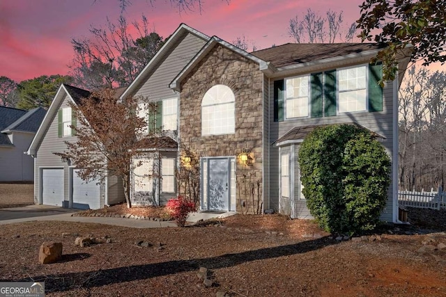 colonial home with stone siding, an attached garage, and concrete driveway