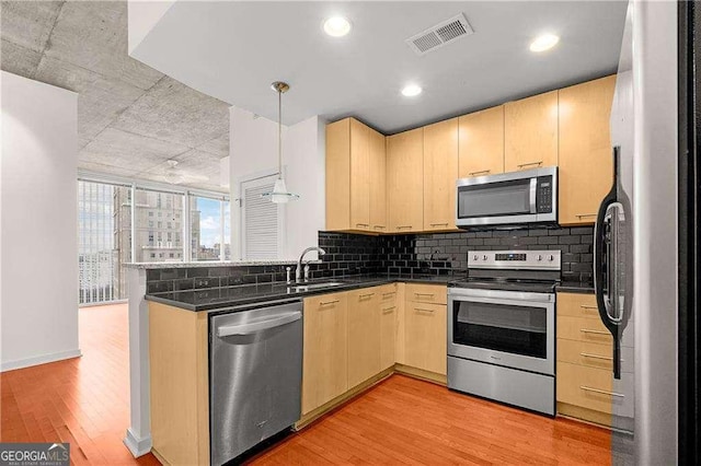 kitchen featuring appliances with stainless steel finishes, pendant lighting, light brown cabinetry, kitchen peninsula, and light wood-type flooring