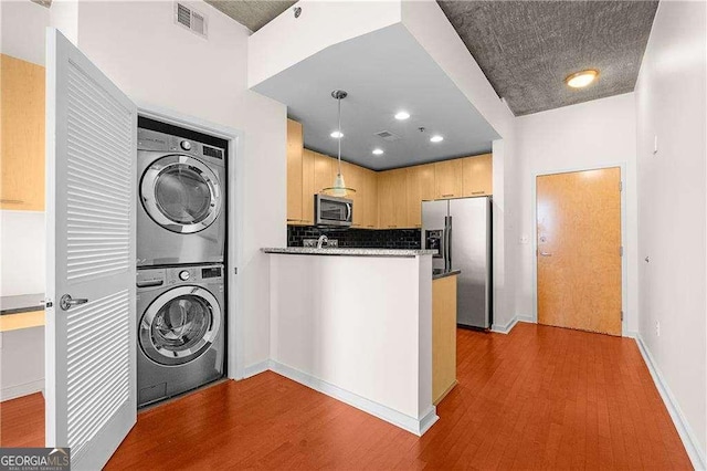 clothes washing area featuring hardwood / wood-style flooring, stacked washer and clothes dryer, and sink