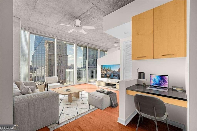 living room featuring ceiling fan, built in desk, expansive windows, and wood-type flooring