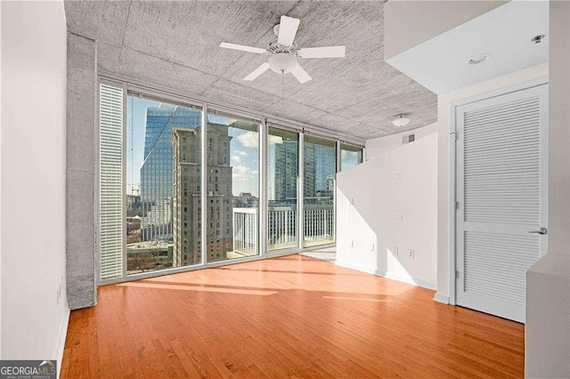 unfurnished room featuring hardwood / wood-style flooring, a wall of windows, and ceiling fan