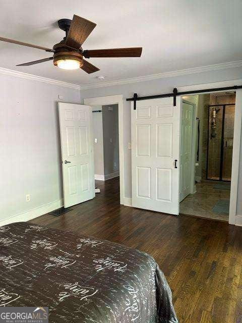 unfurnished bedroom featuring crown molding, dark hardwood / wood-style floors, a barn door, and ceiling fan