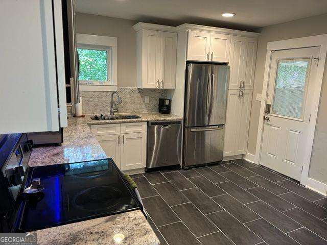 kitchen with stainless steel appliances, light stone countertops, sink, and white cabinets