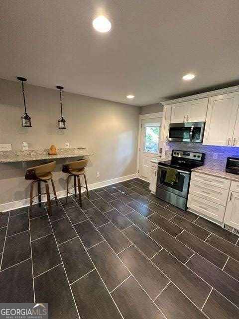 kitchen with appliances with stainless steel finishes, a breakfast bar, white cabinets, hanging light fixtures, and light stone countertops