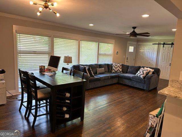 living room with ornamental molding, a barn door, dark hardwood / wood-style flooring, and ceiling fan