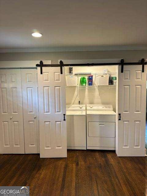 laundry area with ornamental molding, a barn door, washer and dryer, and dark wood-type flooring