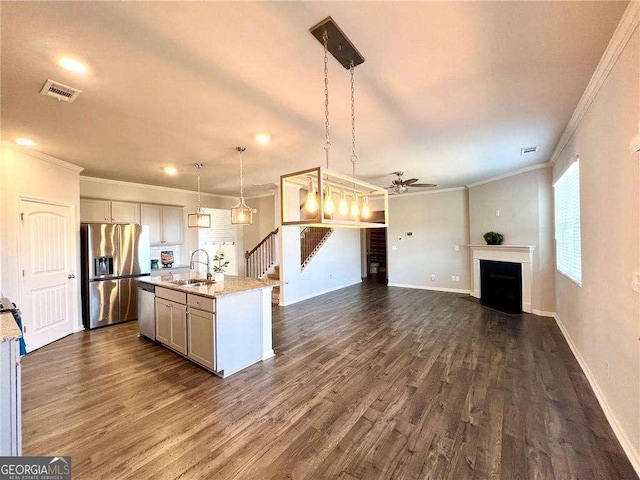 kitchen featuring sink, appliances with stainless steel finishes, light stone countertops, a center island with sink, and decorative light fixtures