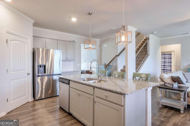 kitchen featuring appliances with stainless steel finishes, sink, hanging light fixtures, a center island with sink, and light wood-type flooring