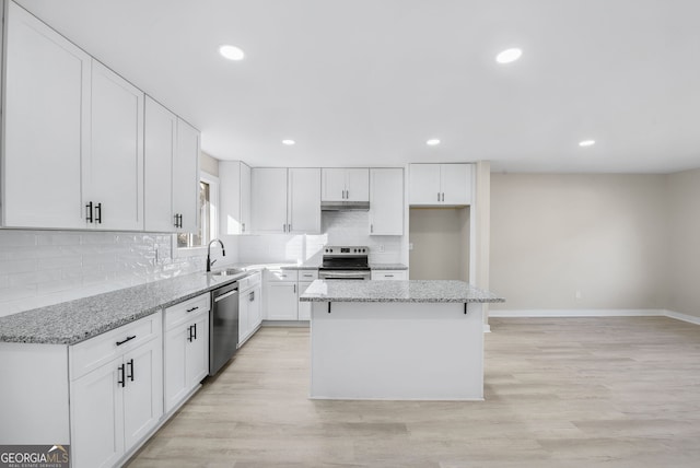 kitchen featuring appliances with stainless steel finishes, white cabinetry, a center island, light stone countertops, and decorative backsplash