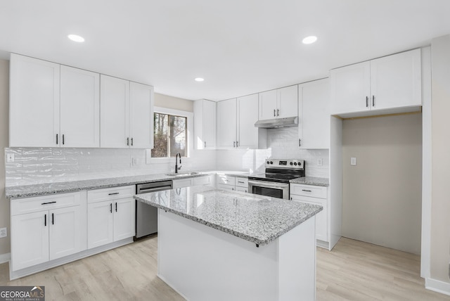 kitchen with sink, light stone counters, a center island, appliances with stainless steel finishes, and white cabinets