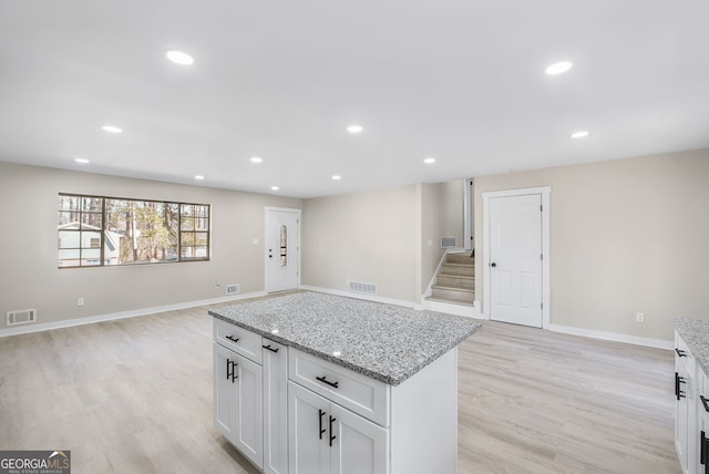 kitchen with a kitchen island, white cabinets, light stone counters, and light hardwood / wood-style flooring