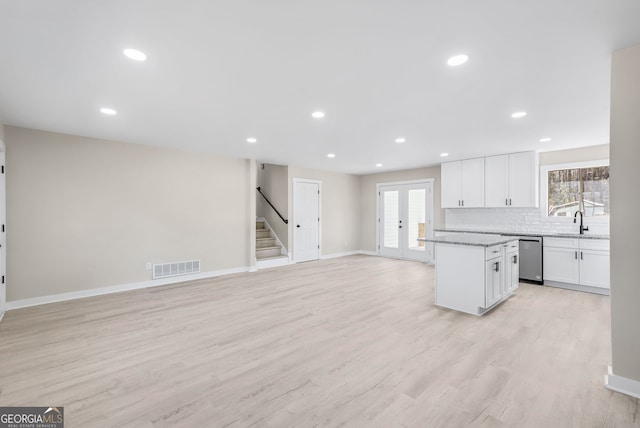 kitchen with white cabinetry, sink, backsplash, stainless steel dishwasher, and light wood-type flooring