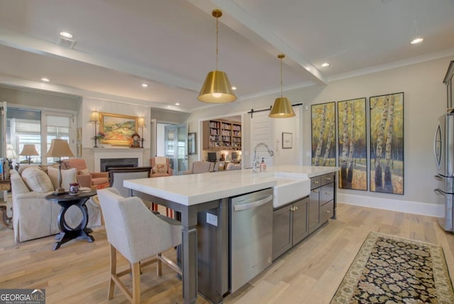 kitchen featuring sink, decorative light fixtures, appliances with stainless steel finishes, beam ceiling, and a kitchen island with sink