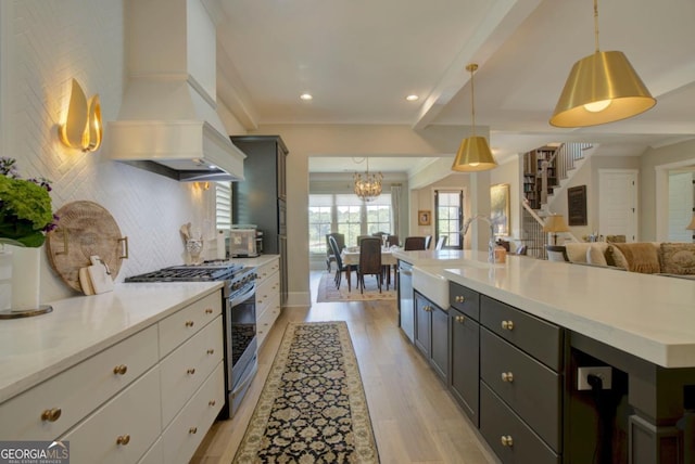 kitchen featuring custom exhaust hood, backsplash, appliances with stainless steel finishes, light wood finished floors, and a sink