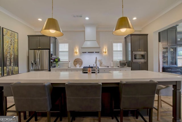 kitchen with gray cabinets, hanging light fixtures, stainless steel appliances, custom range hood, and a kitchen bar