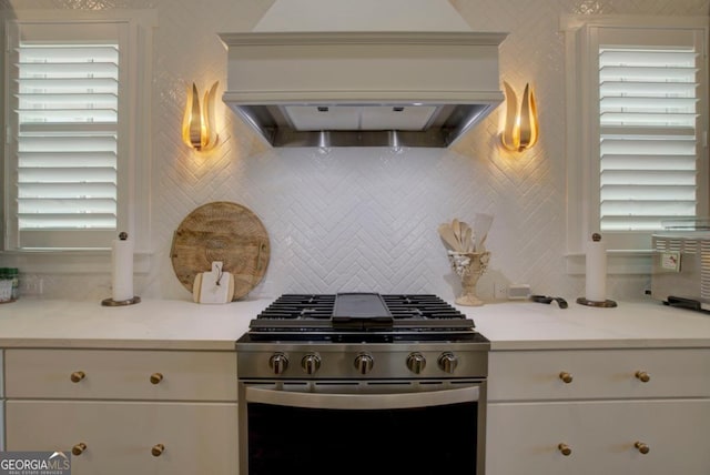 kitchen featuring white cabinets, gas stove, premium range hood, and backsplash