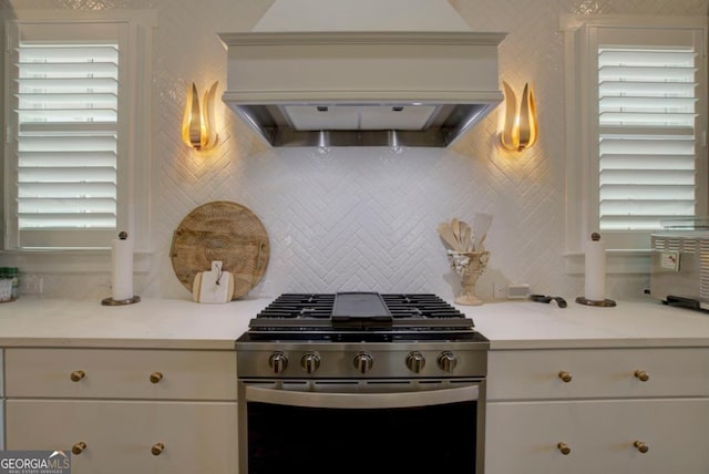 kitchen featuring tasteful backsplash, custom exhaust hood, white cabinetry, light countertops, and gas range