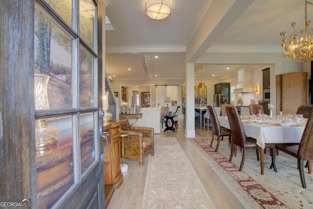 dining area featuring an inviting chandelier, ornamental molding, a barn door, and light wood-type flooring