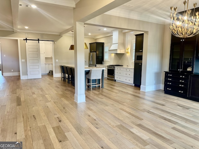 kitchen with crown molding, a breakfast bar, a barn door, stainless steel appliances, and premium range hood