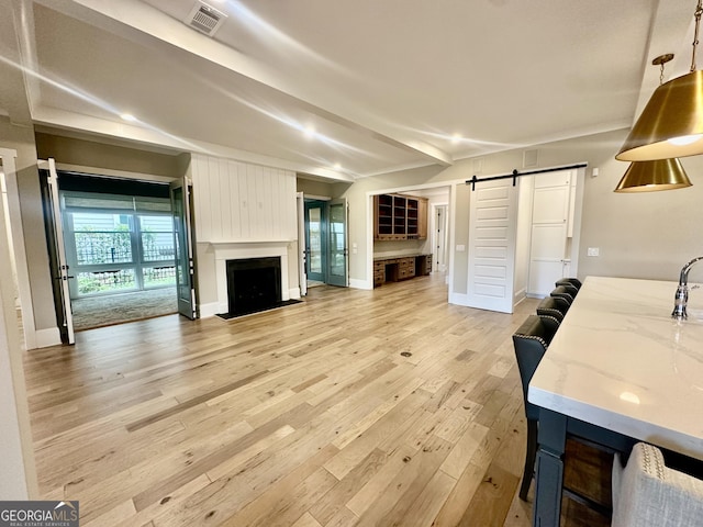 living area with a fireplace, light wood-type flooring, visible vents, a barn door, and baseboards
