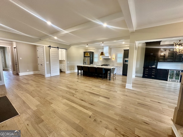 living area featuring light wood-type flooring, beamed ceiling, baseboards, and a barn door