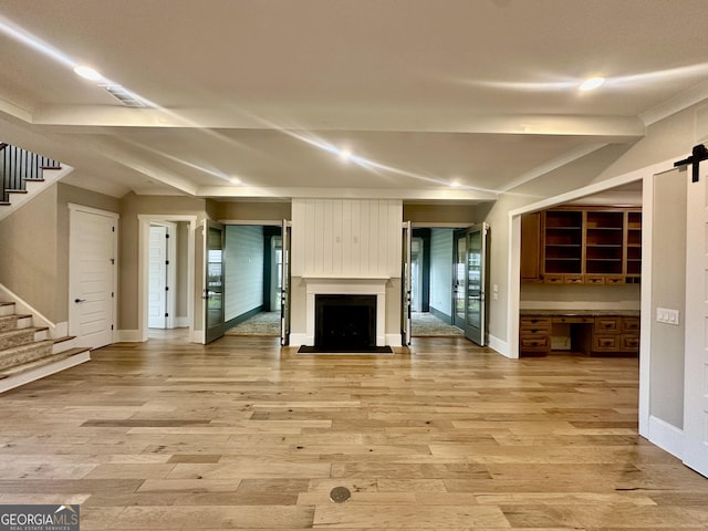 unfurnished living room featuring baseboards, a barn door, light wood-type flooring, a fireplace, and stairs