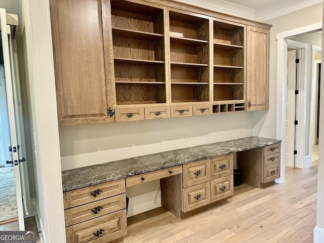 unfurnished office with built in desk, light wood finished floors, and crown molding