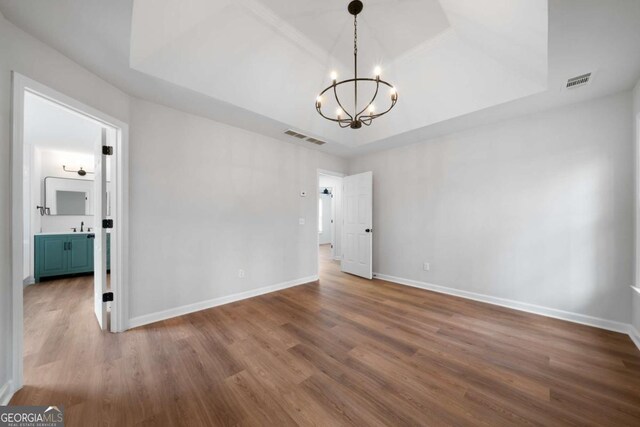 spare room featuring a notable chandelier, sink, wood-type flooring, and a raised ceiling