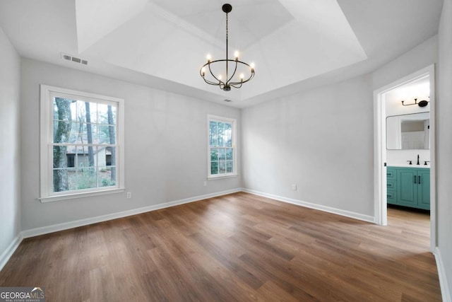 empty room featuring a raised ceiling, hardwood / wood-style flooring, sink, and an inviting chandelier