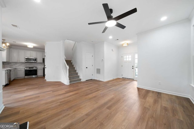 unfurnished living room featuring ceiling fan with notable chandelier and light wood-type flooring