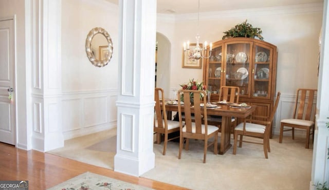 dining space featuring ornate columns, crown molding, light wood-type flooring, and an inviting chandelier