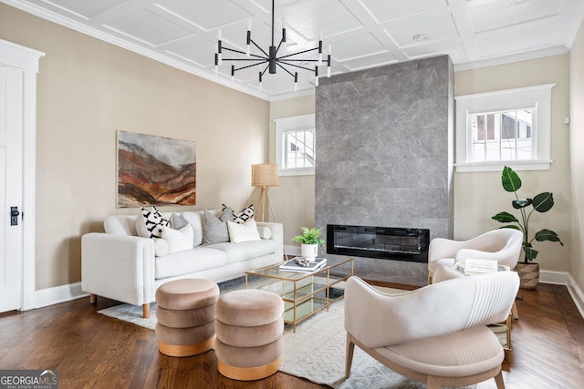 living area with a tiled fireplace, coffered ceiling, wood finished floors, baseboards, and a chandelier