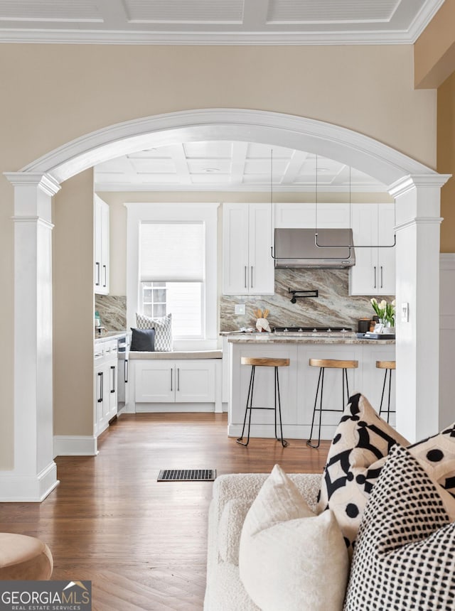 living area featuring light wood-type flooring, visible vents, ornamental molding, arched walkways, and decorative columns