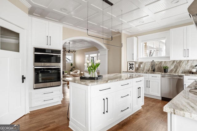 kitchen with stainless steel appliances, arched walkways, backsplash, and wood finished floors