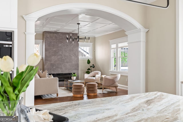 bedroom featuring wood finished floors, arched walkways, a premium fireplace, decorative columns, and baseboards