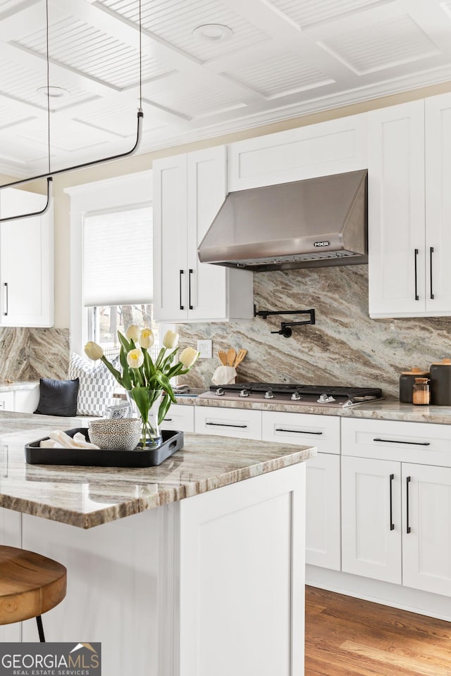 kitchen featuring under cabinet range hood, stainless steel gas cooktop, white cabinetry, and light stone countertops