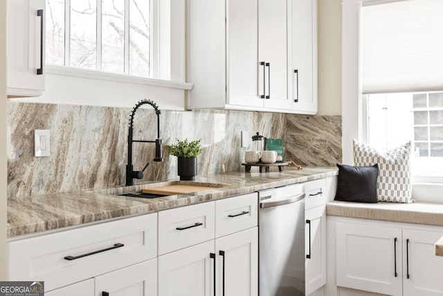 kitchen with a sink, backsplash, stainless steel dishwasher, white cabinetry, and light stone countertops