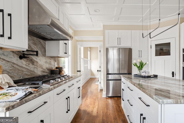 kitchen with ventilation hood, decorative backsplash, appliances with stainless steel finishes, wood finished floors, and white cabinetry