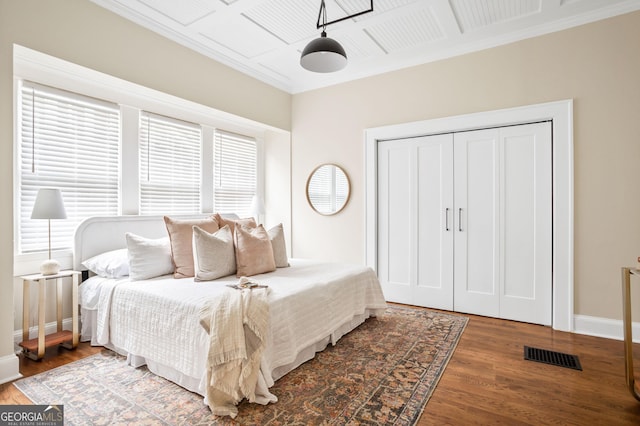 bedroom featuring visible vents, crown molding, baseboards, wood finished floors, and a closet