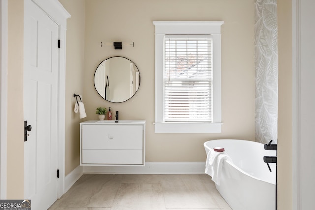 bathroom with vanity, a soaking tub, and baseboards