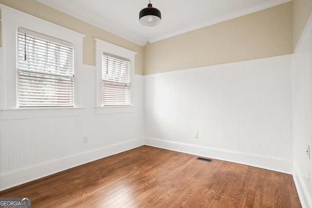 unfurnished room with crown molding, wood finished floors, a wainscoted wall, and visible vents