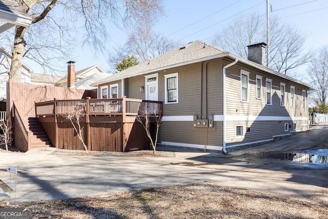 rear view of house featuring a chimney, driveway, roof with shingles, a wooden deck, and stairs