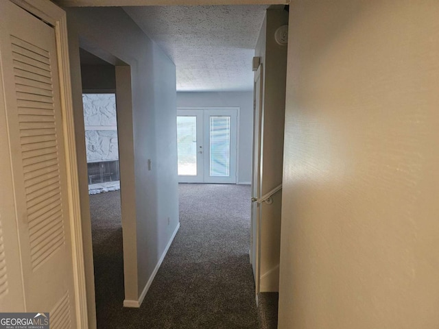 hallway featuring french doors, a textured ceiling, and dark colored carpet