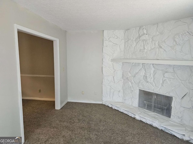 unfurnished living room with dark colored carpet, a stone fireplace, and a textured ceiling